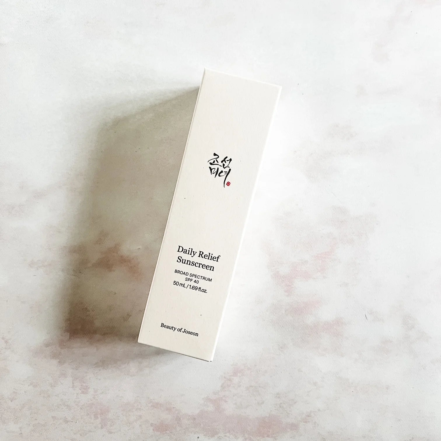 Tall white box labeled 'Daily Relief Sunscreen' on a textured beige surface